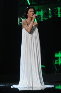 Anastasia Prikhodko sings on stage wearing a white full length dress at the ESC in Russia