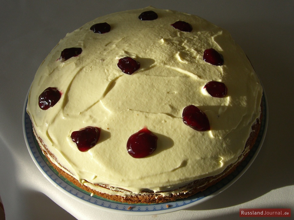 Покрытый белым кремом и украшенный капельками красного варенья торт Трухлявый пень
