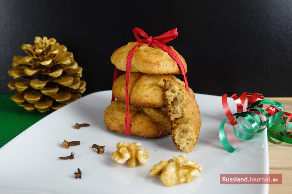 Drei Lebkuchen aufeinander gebunden mit roter Schleife auf weißem Teller mit Walnüssen und Nelken