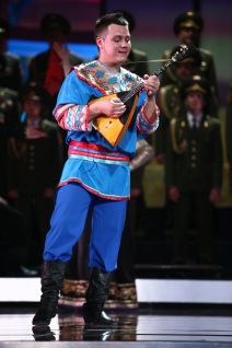 Man in blauer russischer Nationaltracht spielt Balalaika vor dem Chor des Alexandrow Ensembles der Russischen Armee