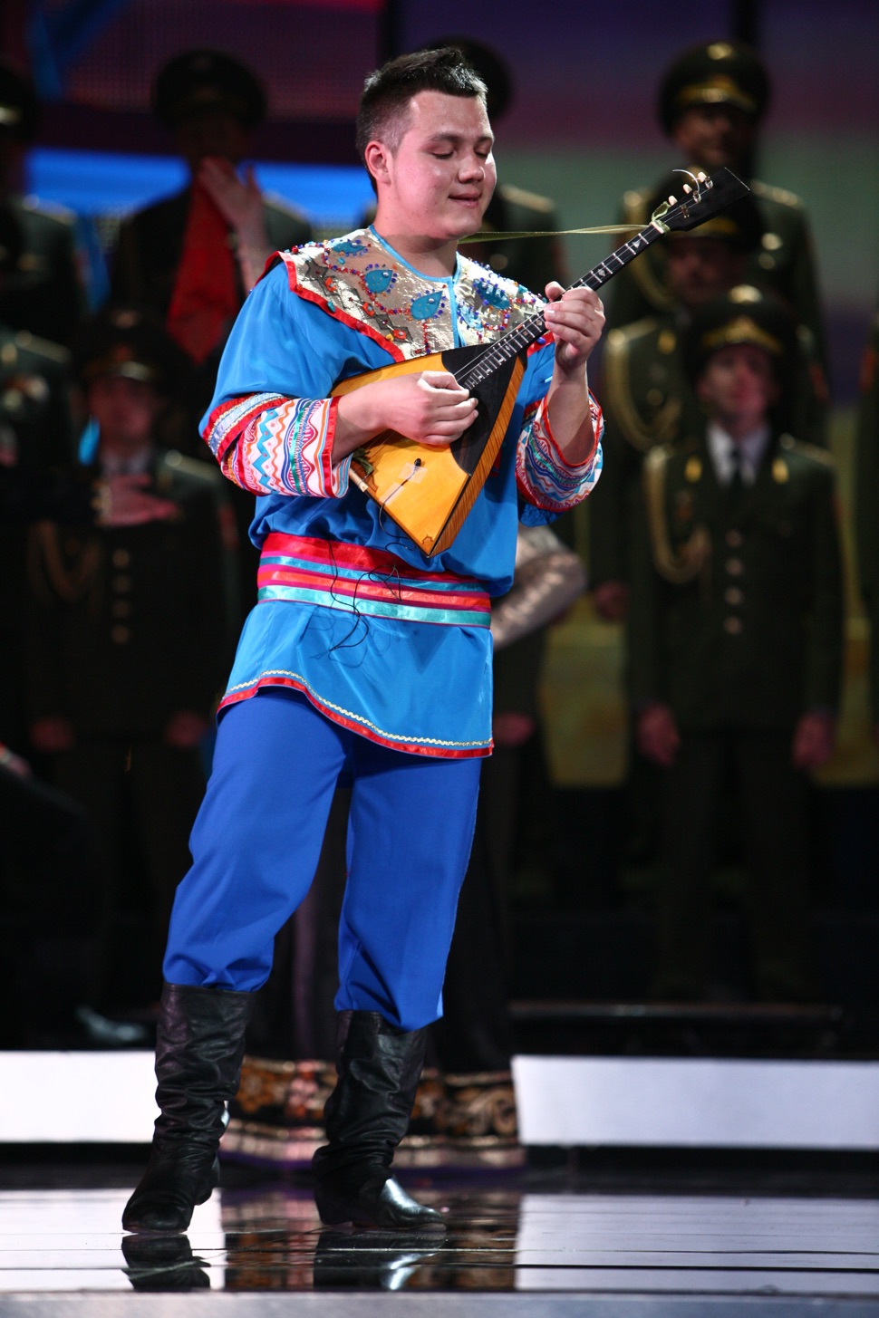 Man in blauer russischer Nationaltracht spielt Balalaika vor dem Chor des Alexandrow Ensembles der Russischen Armee