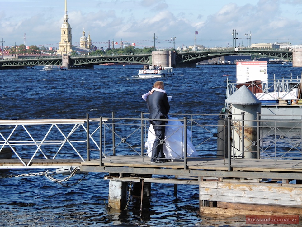 Brautpaar umarmt sich auf einem Holzsteg an der Newa vor Peter-Paul-Festung in St. Petersburg