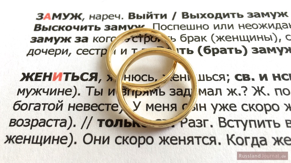 Zwei Eheringe auf dem russischen Text mit Vokabeln zum Heiraten