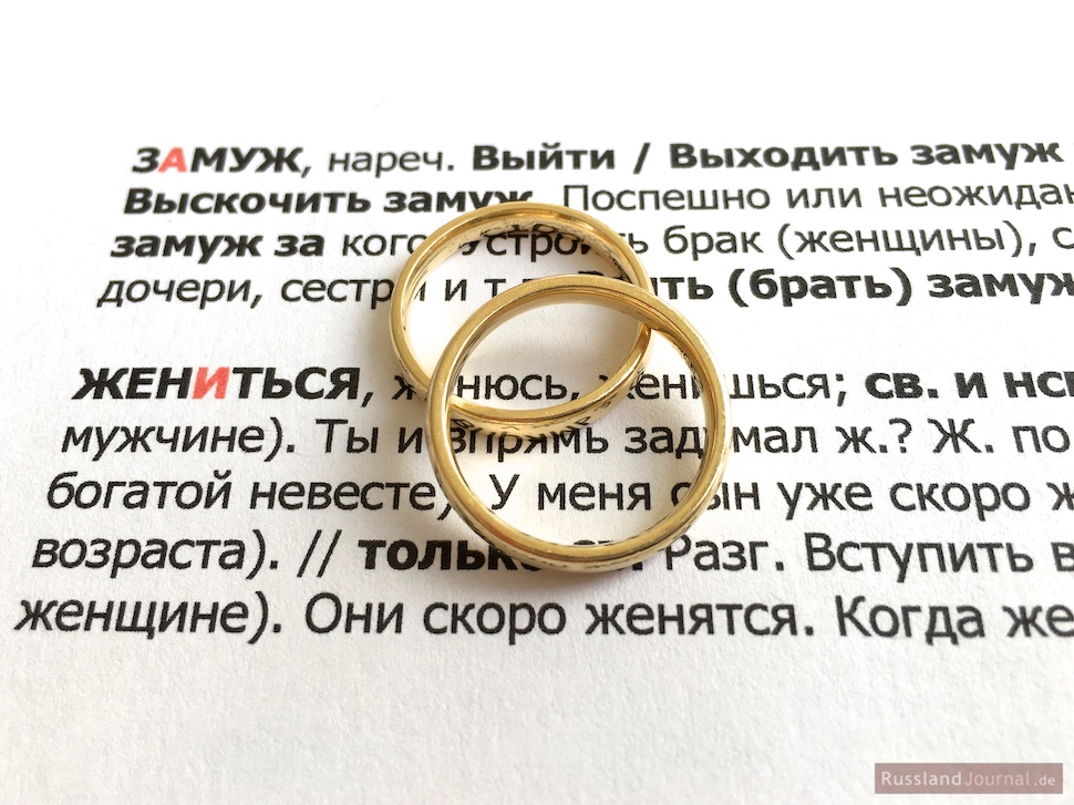 Zwei Eheringe auf dem russischen Text mit Vokabeln zum Heiraten