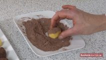 Hand wälzt Kartoschka in der Kakao-Puderzucker-Mischung